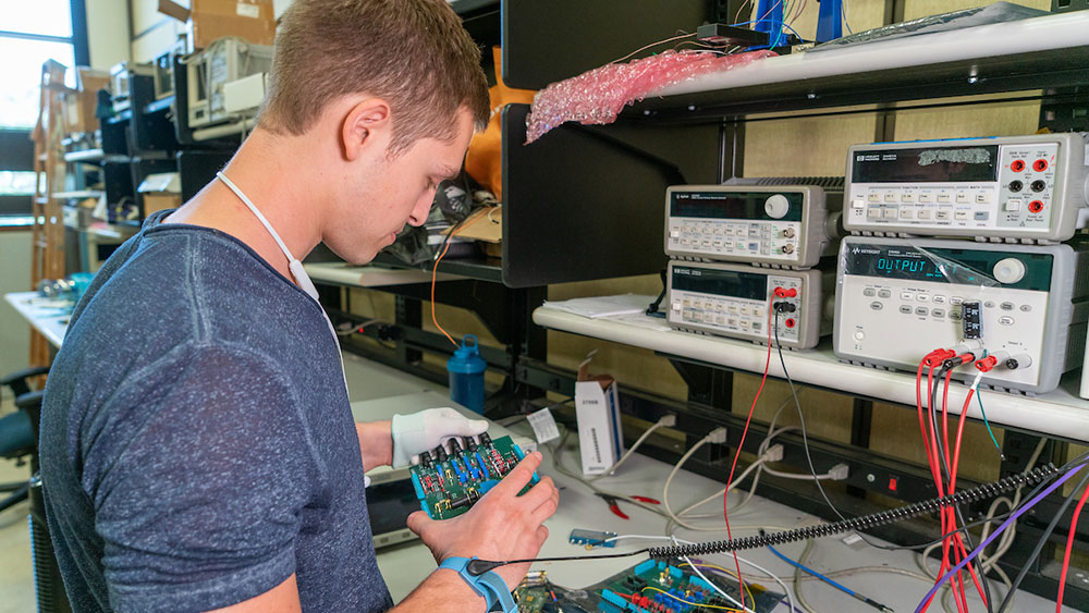 student working on a circuit board in an electronics lab