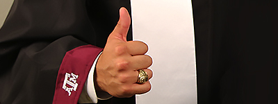 Student in graduation gown with Gig 'em sign