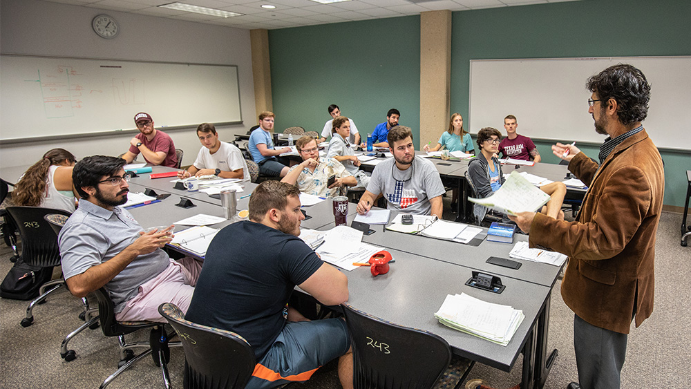 A professor stands in front of a class full of students for a lecture.