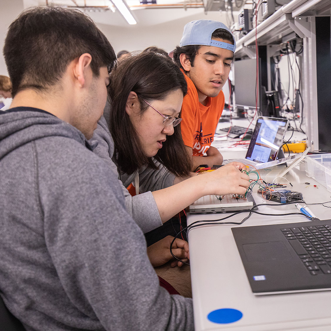 Two male students watch as a female student works on an engineering project in a Zachry building lab.