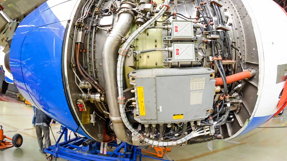 Person troubleshooting an aircraft engine with the hood open, in an aircraft hangar.