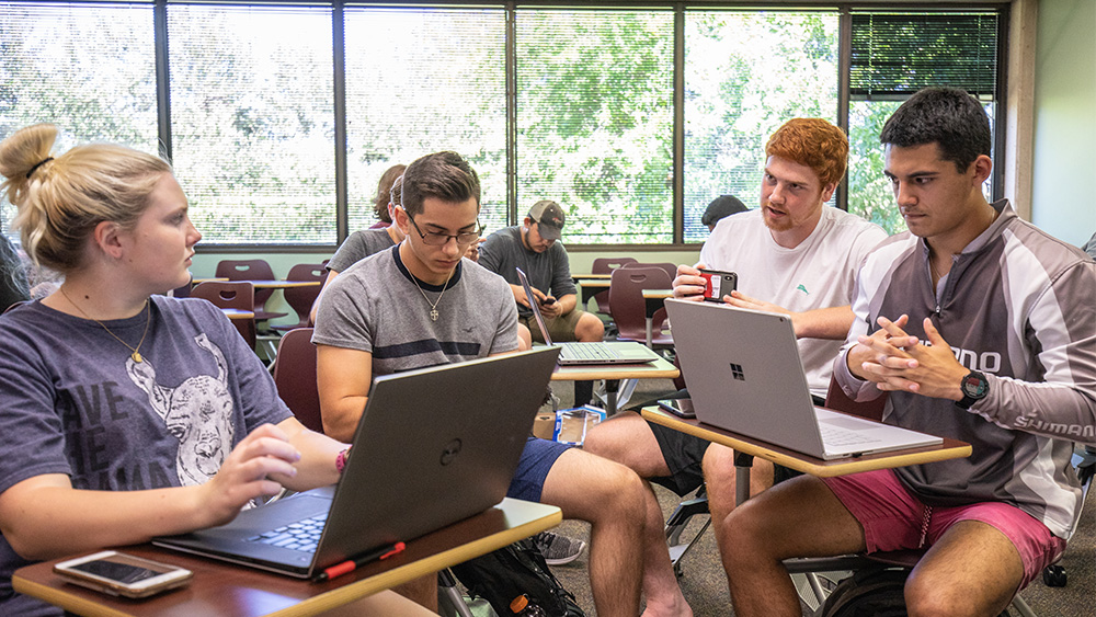 Four students sit at their desks and talk