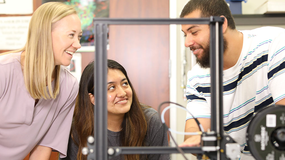 Two females and a male standing in front of lab equipment