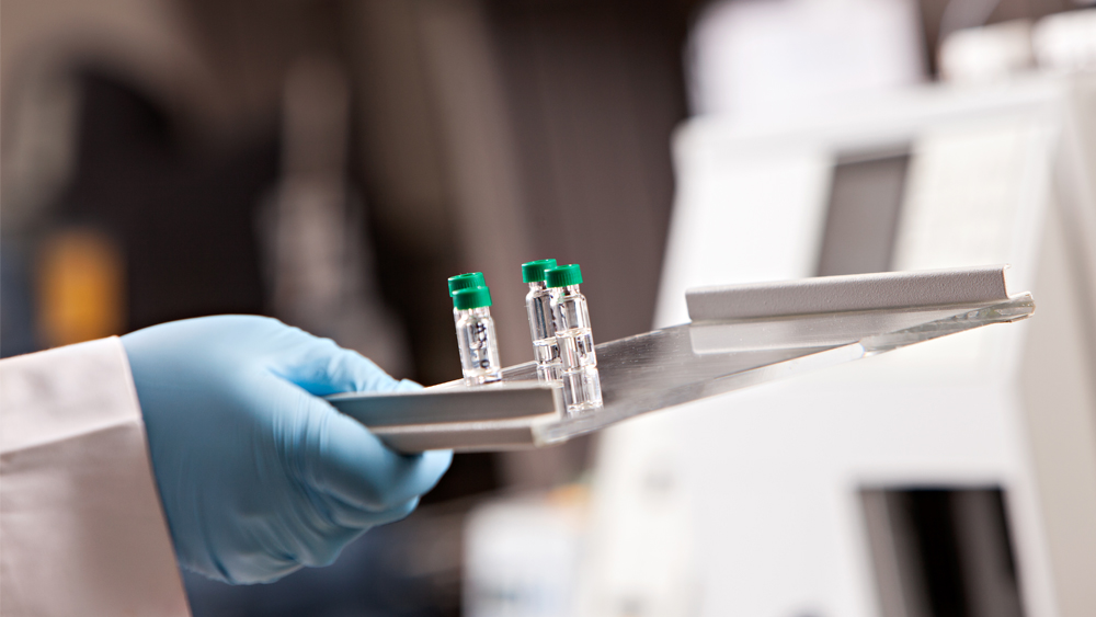 Three vials of liquid on a tray being held by a gloved hand.