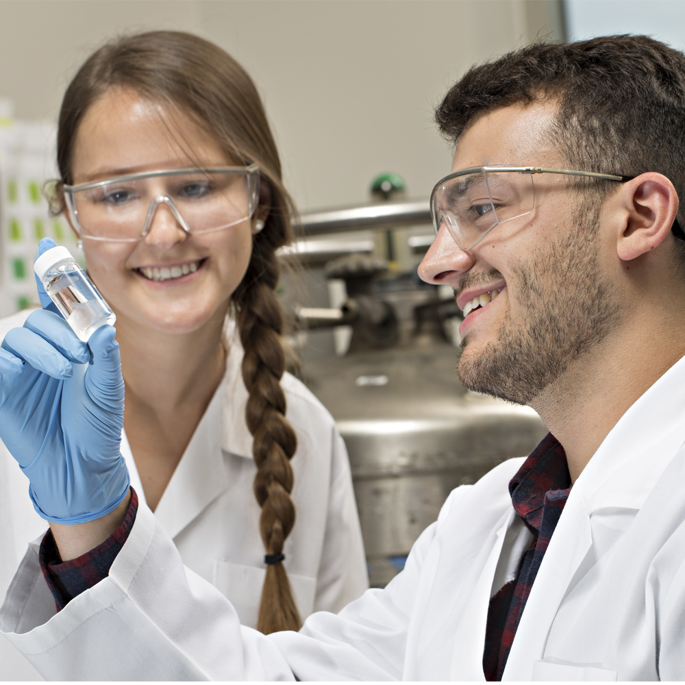 Two students, one female and one male, look at vial full of material. They are in a lab space.