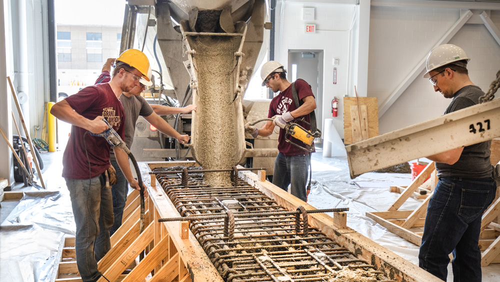 People in hard hats work on creating concrete columns 