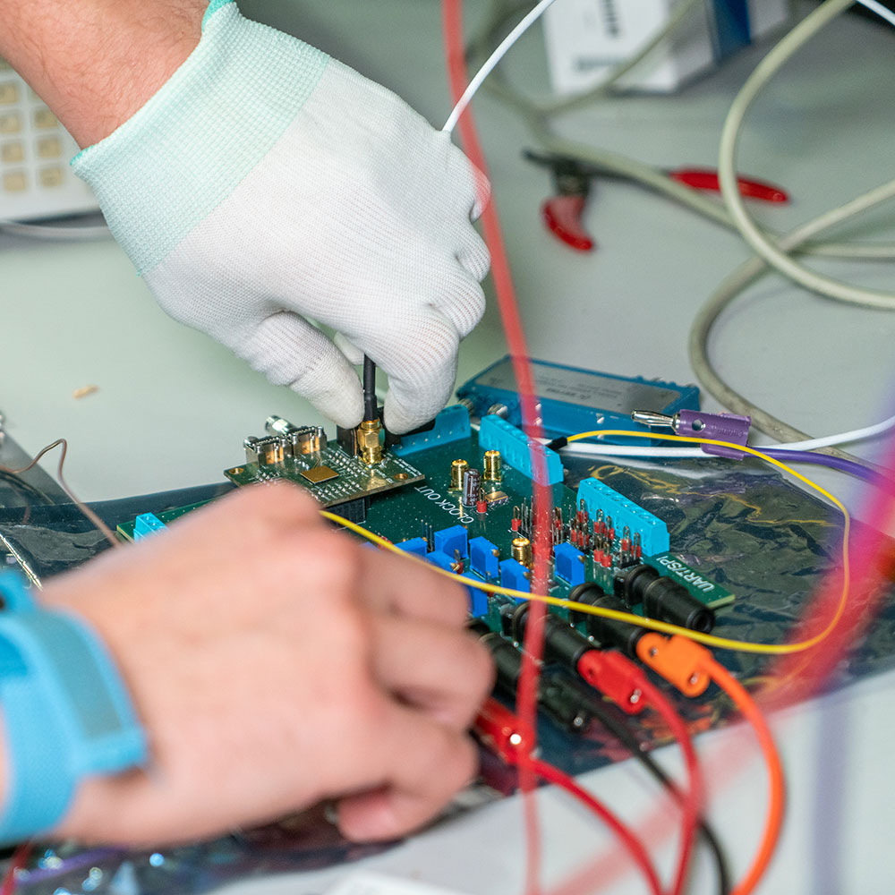 Hand with gloves holding wires connected to integrated circuit on a desk