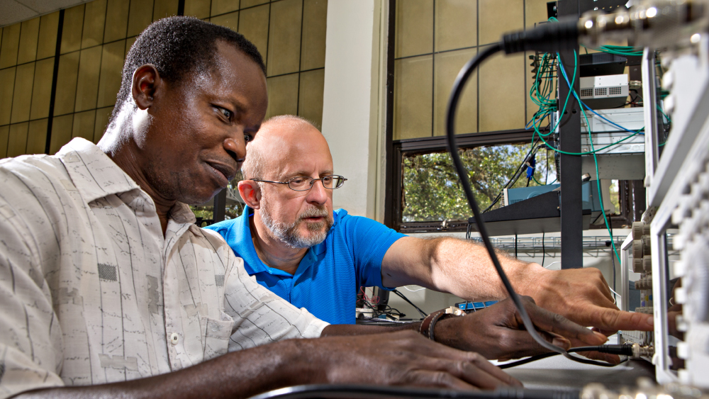 Faculty member helping a graduate student with some electrical equipment.