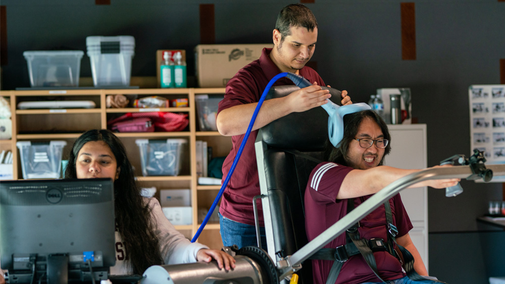 Three students work with a robotic arm in the lab.