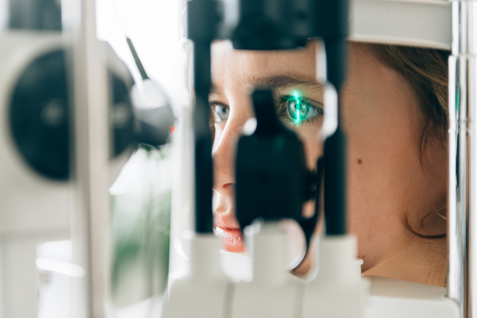 Close up of woman looking into eye equipment at optometrist. Thin line of green light is reflected on her right eye.