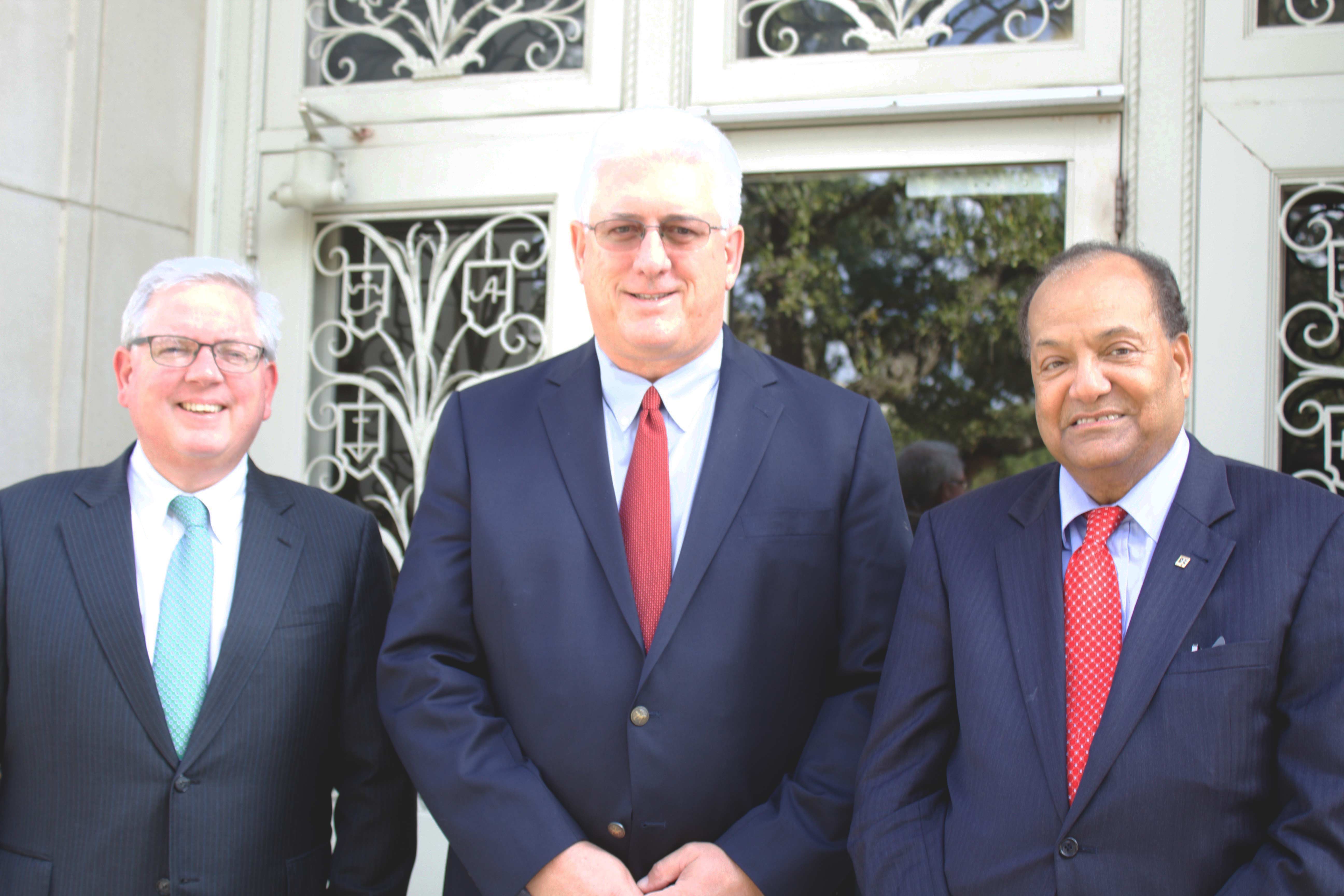 Three men in dark blue business suits standing in from of wrought iron doors.