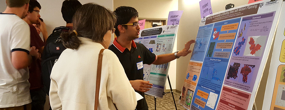 Male student showing woman poster with his research on it. There is another poster beside him with a group of boys standing around it.