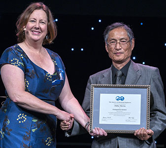 Janeen Judah and Nobuo Morita share handshake as Morita holds framed award