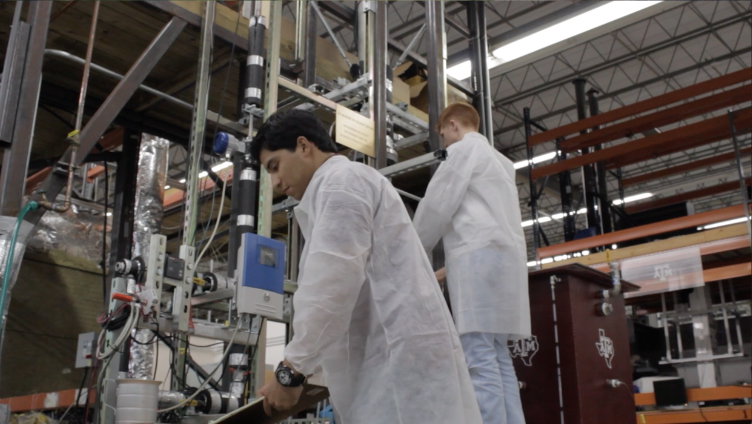 Two males students in lab working with equipment. They're both wearing slightly translucent white lab coats.