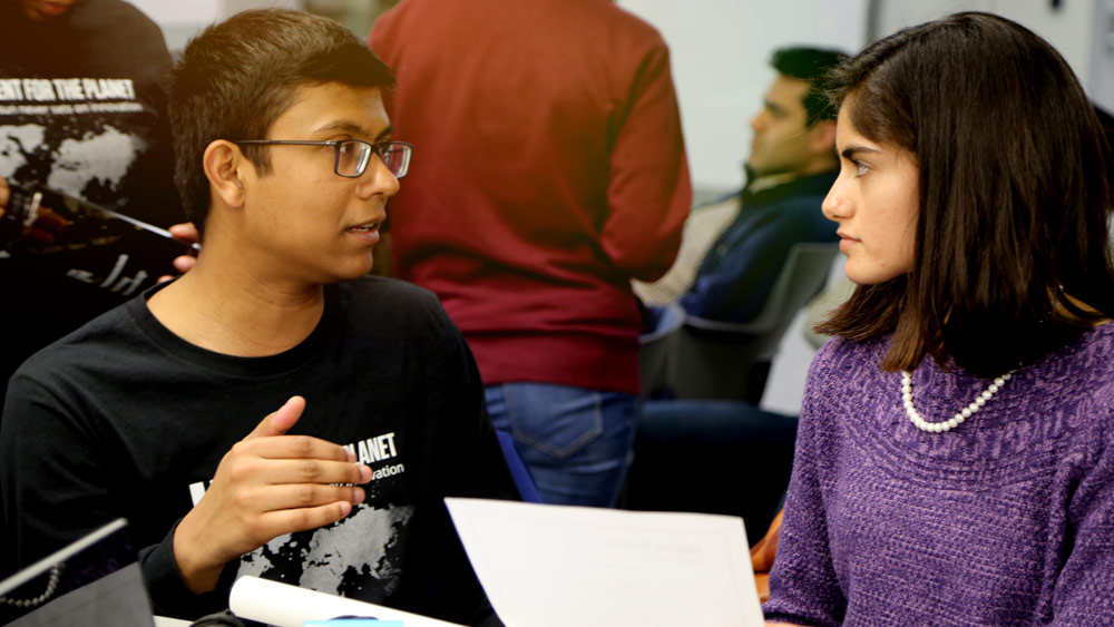 Two students discuss a project challenge while looking at a paper during Invent for the Planet.