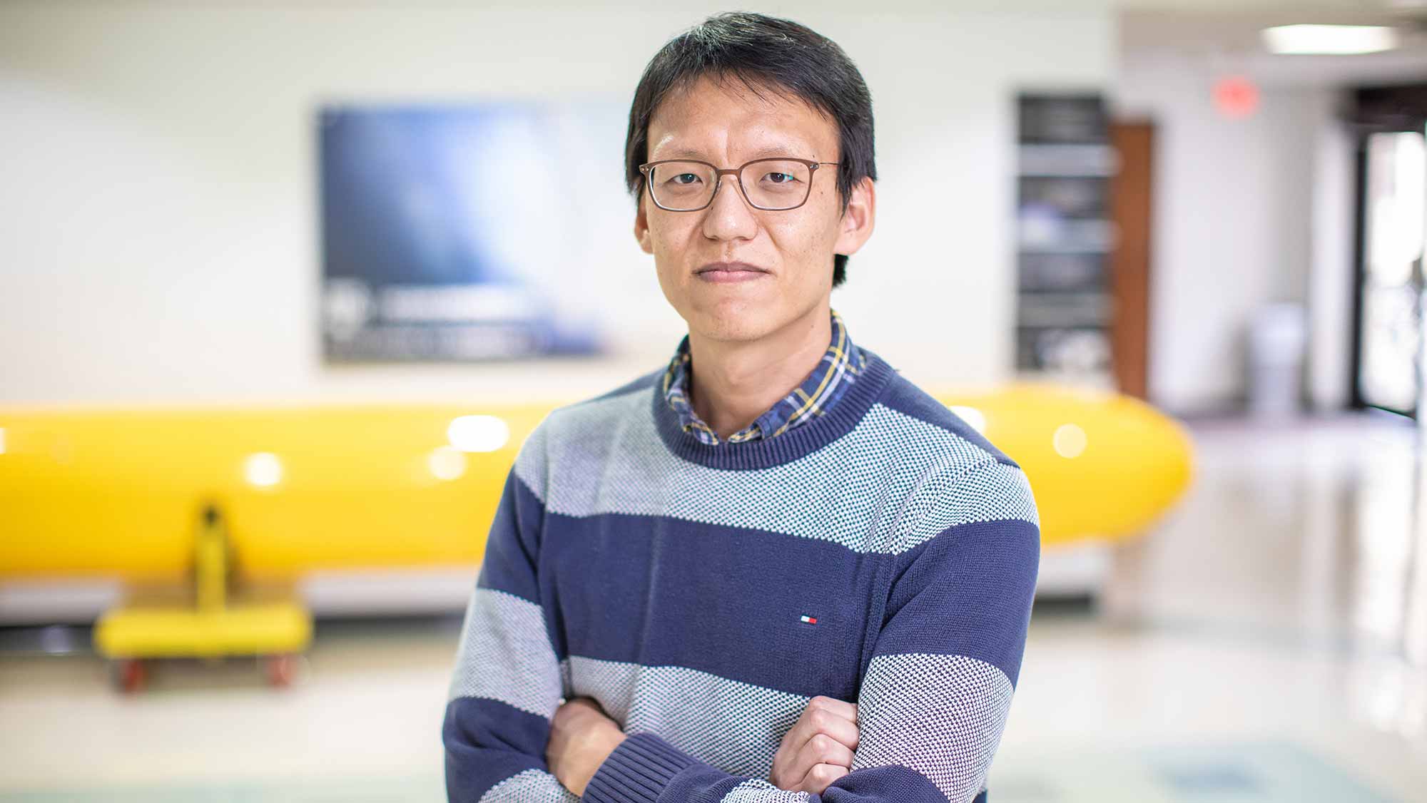 Kang stands with folded arms in the lobby of the Haynes Engineering Building.