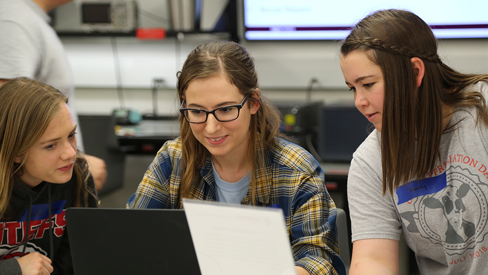 Three female students look at computer screen during design event.