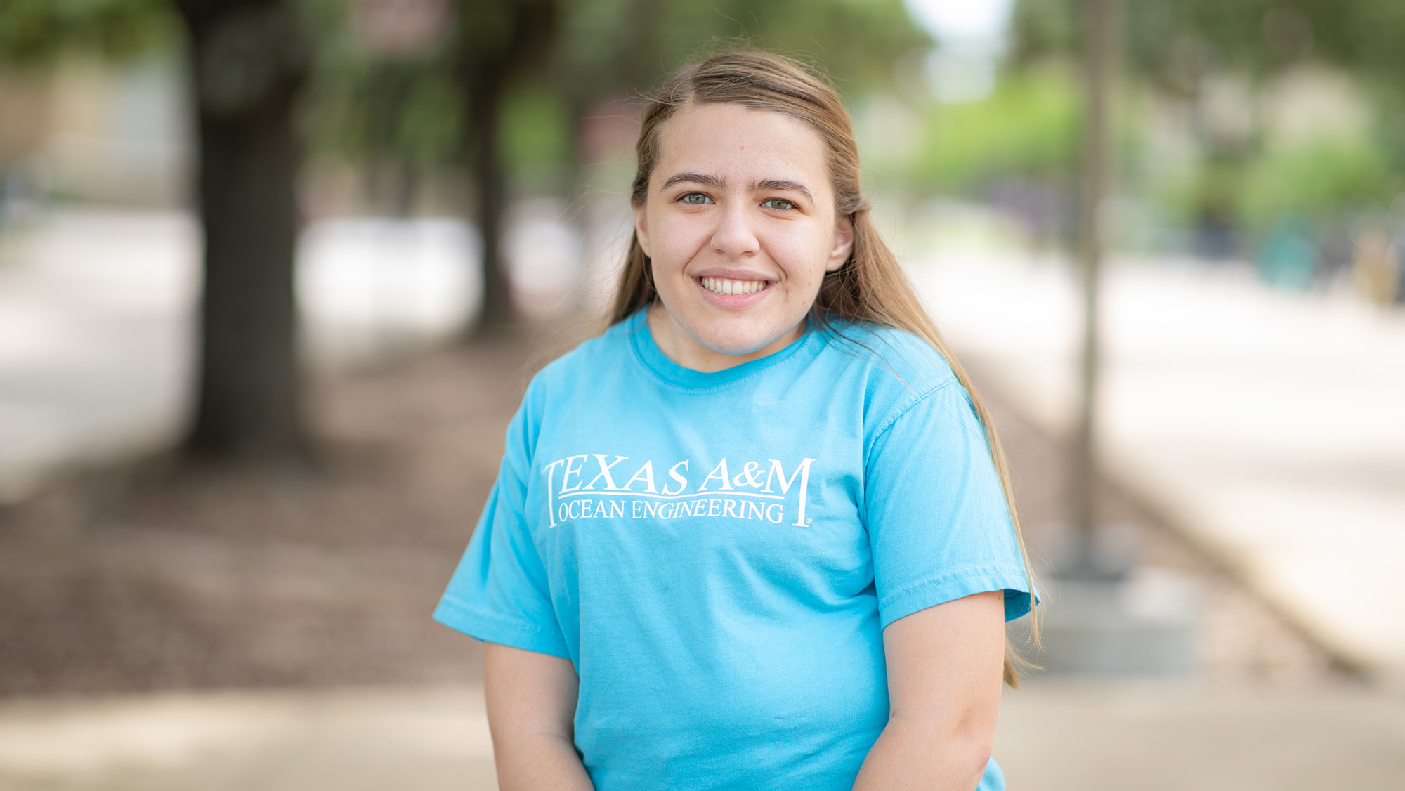 Patricia Rodriguez poses under the trees on sunny day wearing a blue ocean engineering shirt.