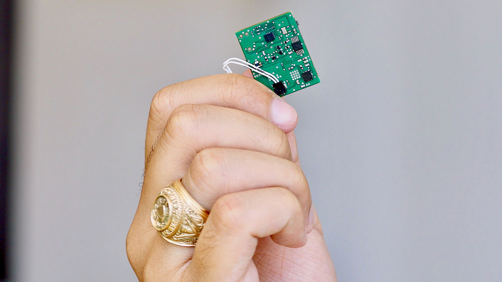 Student with Aggie ring holding up the chip that powers the Swing Sleeve invention they have created.