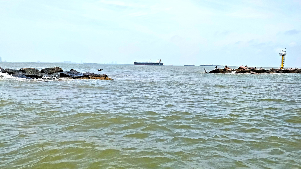 A look over the open ocean water with rock barriers and a ship in the distance.