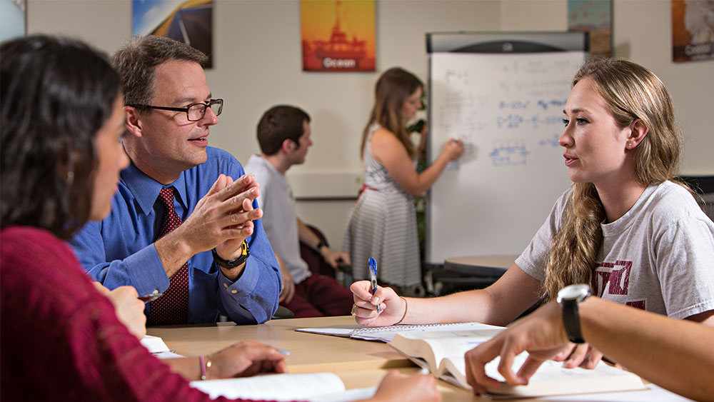 Two students sitting down and talking with a professor.