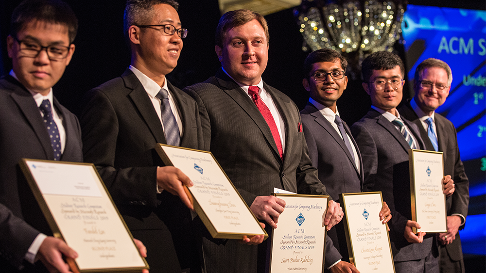 Graduate student Scott Kolodziej (center) stands on stage holding his award with other winners. 