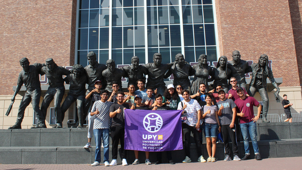 A group of students stand in front of the Aggie War Hymn statue