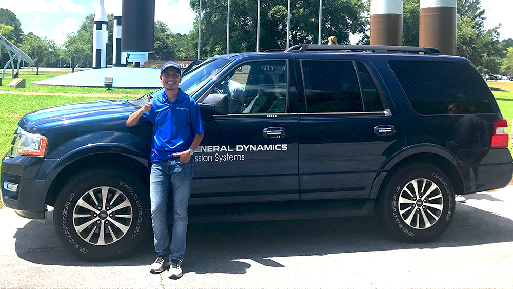 Eddie Chavez smiling next to General Dynamics Mission Systems van.