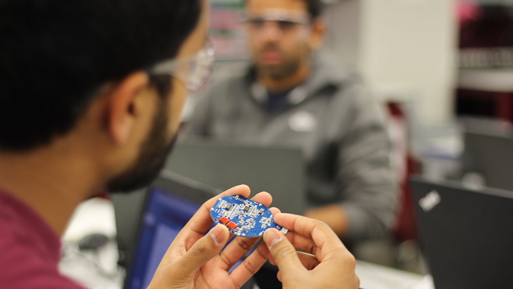 Male student with safety glasses holds his processor part of his innovation where he works in the design center. 