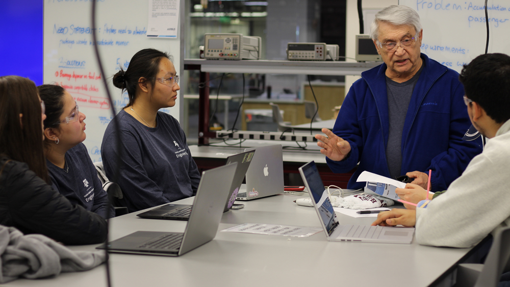 Four students sit at a table with their laptops and listen to a mentor during the Invent for the Planet competition.