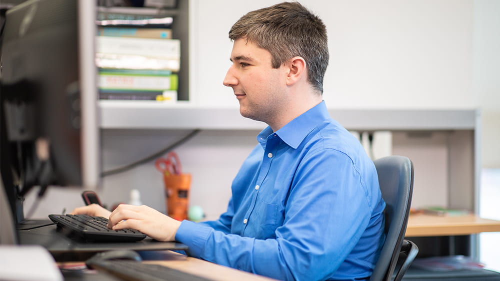 Student sits at a desk while typing on a keyboard in front of a computer. 