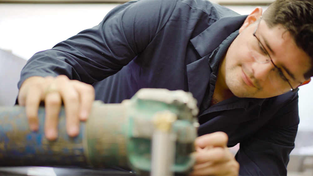 Enrique Losoya inspects drill bit for wear in petroleum engineering lab at Texas A&M University