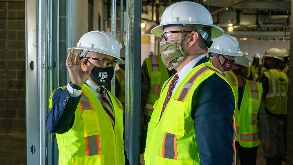 Ross Guieb talking to Ryan D. McCarthy during a tour at the Research Integration Center, with both wearing hard hats, construction vests and masks. 