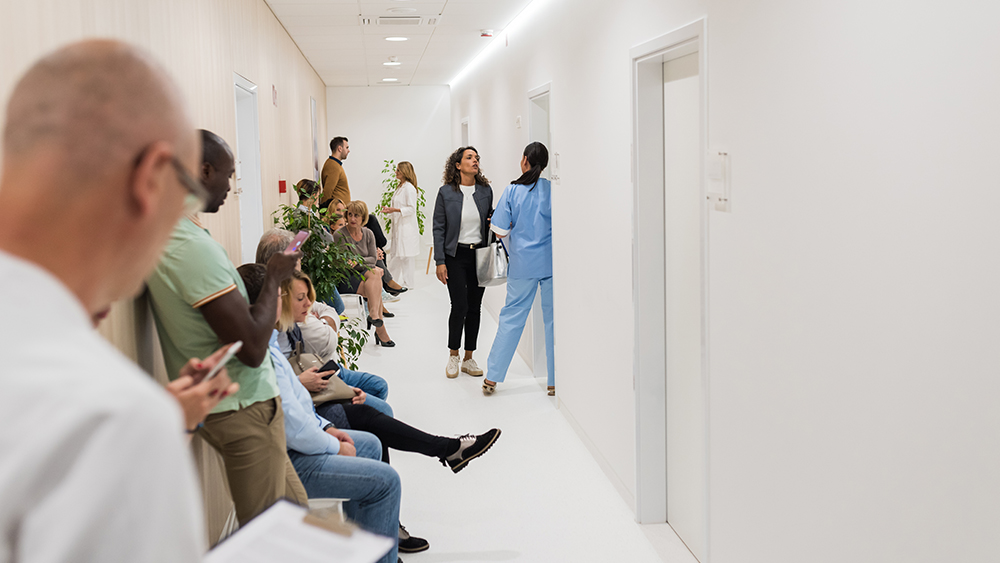 A group of people are crowded in a hallway as they wait around. Some people are standing, some are on cell phones and some are talking to each other.