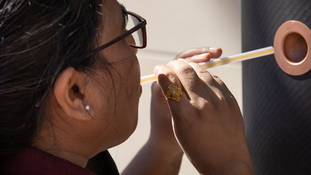 A girl blowing through a straw into the new COVID-19 breathalyzer.