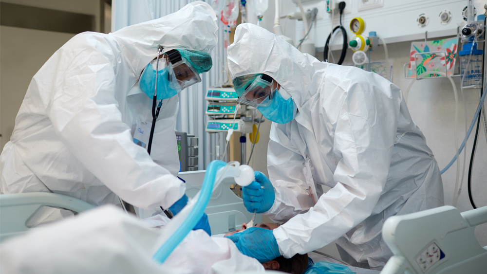 Two hospital staff work to intubate a patient lying on a hospital bed.