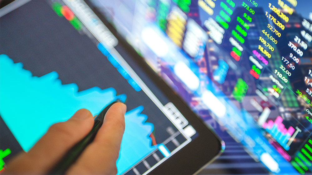 A hand in from of a monitor showing tabulated data.