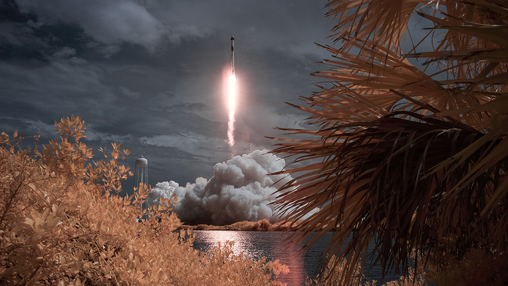 The SpaceX Falcon 9 rocket launches into the Florida sky as seen from across a bay.