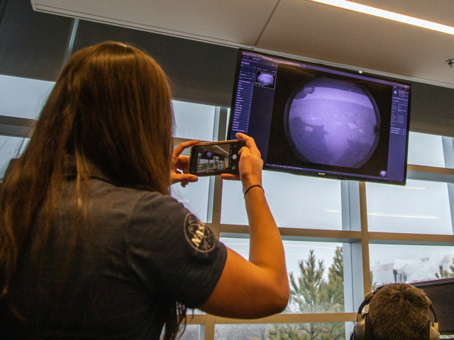 Santini De León taking a picture of a monitor projecting the Perseverance rover's view on Mars.