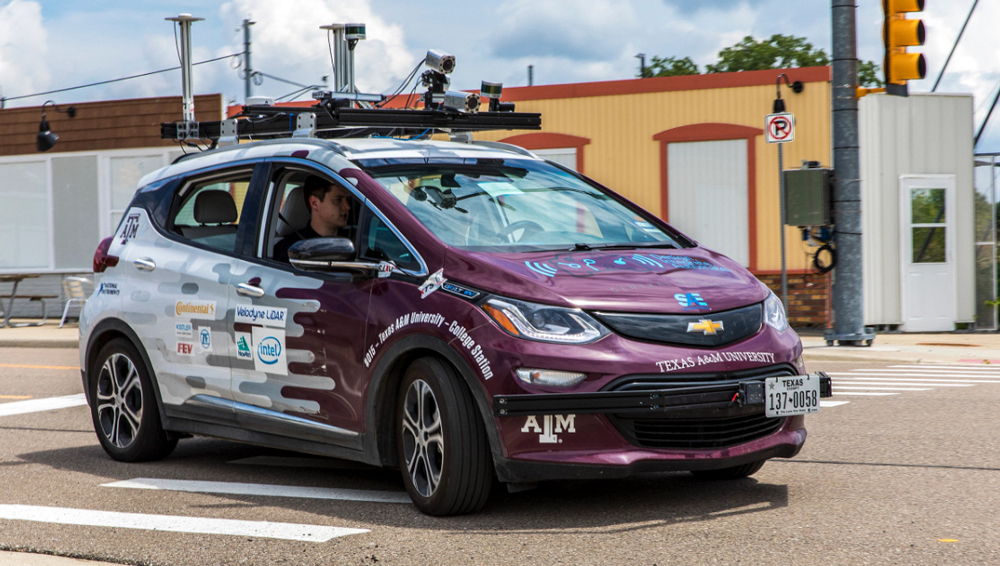 Two members of the Texas A&amp;M AutoDrive team behind the wheel of their autonomous car driving on a test course.