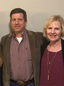 Yvonne and Kevin Newman posing for a photo in front of a wall. 