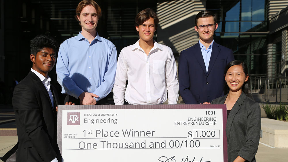 Five members of first-place team Jacket holding a large sign representing a check awarded to them for $1,000