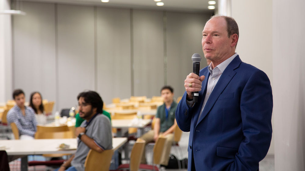 Jim Wilkes using a microphone to speak to listening students.