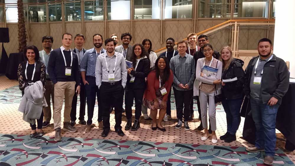 Ashley Saquic Tax stands with a group of 18 symposium attendees in a hotel lobby. 