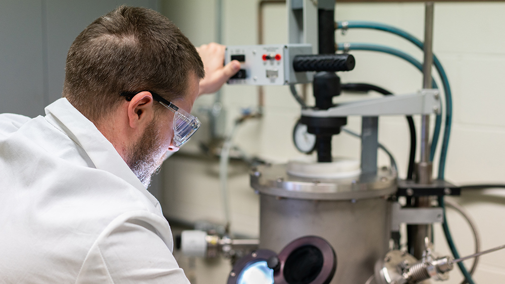 Male scientist looking into a piece of equipment for research purposes. 