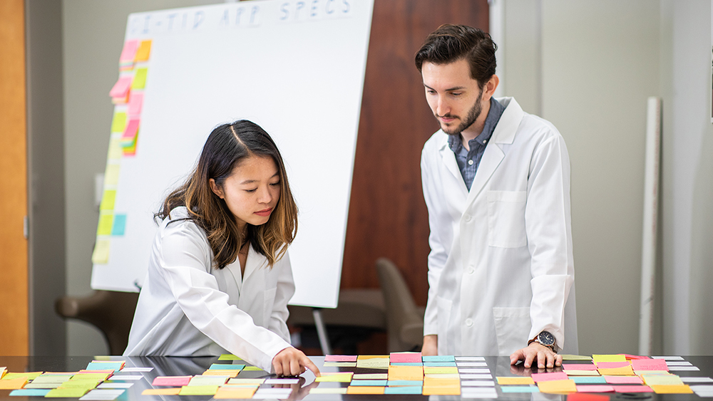 Master of Engineering students stand at a table wearing white lab coats.