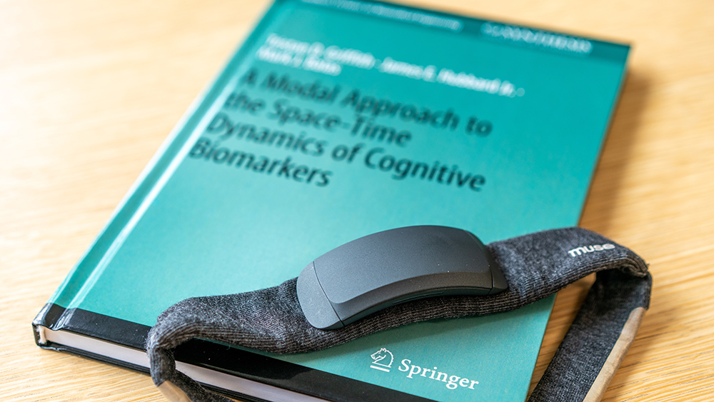 The book titled "A Modal Approach to the Spac-Time Dynamics of Cognitive Biomarkers" with a headband device resting on top of it. 