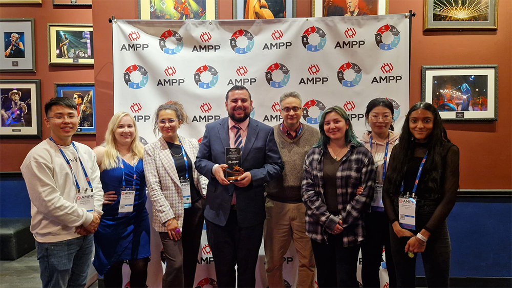 Alan Martinez holds his award and stands next to Dr. Raymundo Case (right of Martinez) and six members of the corrosion lab at Martinez’s award ceremony. 