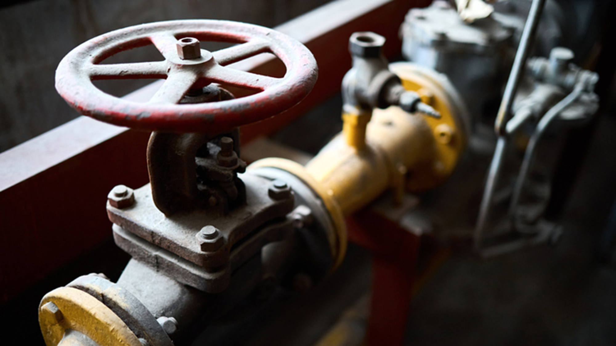 Image of a yellow pipe that has a red wheel to turn it on and off.