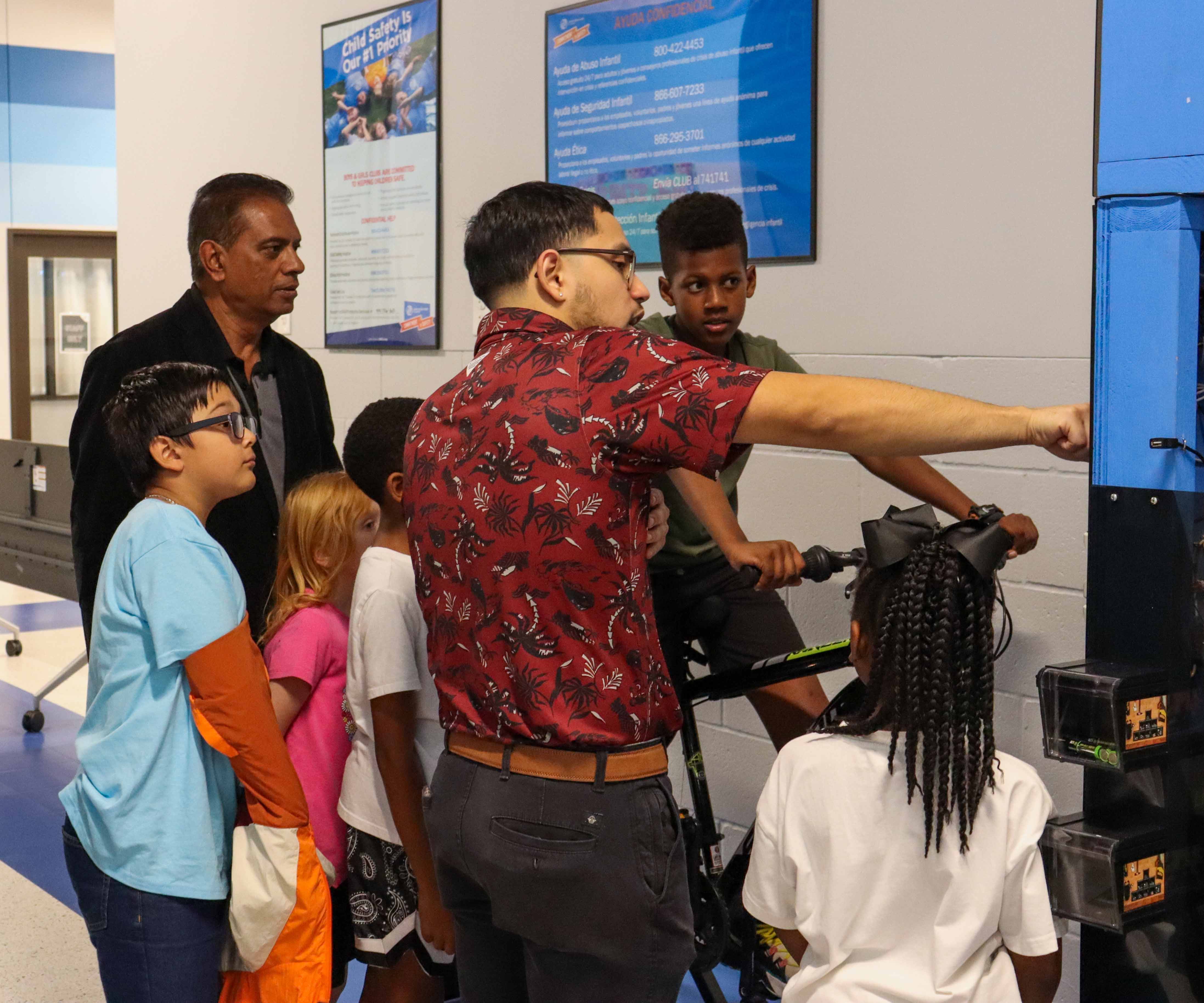 A child is riding a bike that is hooked up to a generator, while two men explain what the bike does. 